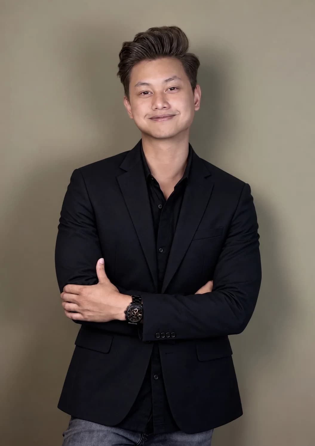 Eddy in a black blazer, arms crossed, against a warm grey backdrop